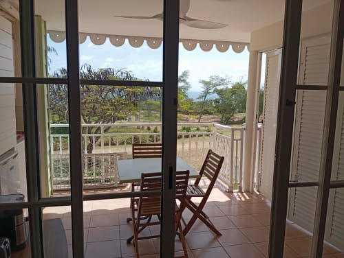 Vue depuis le balcon de la suite Tropic Apartments à Sainte-Anne, Guadeloupe : vue mer, chaises en bois et jardin tropical