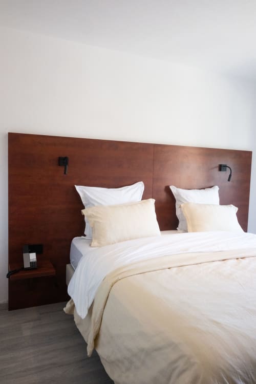 Chambre de l'hôtel La Joya à Cavalaire-sur-Mer avec un lit king-size, literie crème et blanche, tête de lit en bois