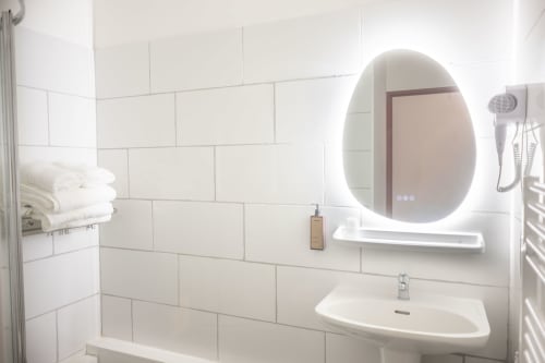 Salle de bain moderne de la Chambre Familiale de l'hôtel La Joya, Cavalaire-sur-Mer, avec carreaux de métro blancs et miroir ovale illuminé