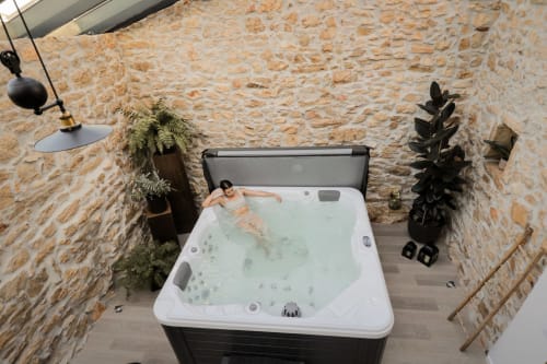 Hôte se relaxant dans un bain à remous extérieur à Recantos D'Almerinda, entouré de murs en pierre rustique et de plantes à Pombal, Portugal