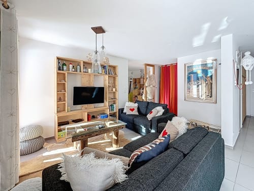 Salon contemporain de l'appartement de Montgenèvre avec canapés foncés, meuble TV en bois et rideaux rouges surplombant les montagnes