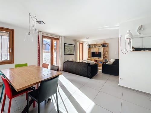 Séjour ouvert dans l'appartement de Montgenèvre avec table à manger, canapé noir, étagères en bois et vue sur les montagnes