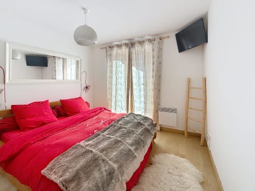 Chambre lumineuse avec literie rouge vif, échelle en bois, rideaux beiges, TV et vue sur les montagnes à Montgenèvre.