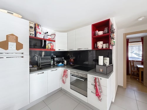 Cuisine moderne dans l'appartement de Montgenèvre avec armoires blanches, étagères rouges, comptoirs noirs et appareils inoxydable