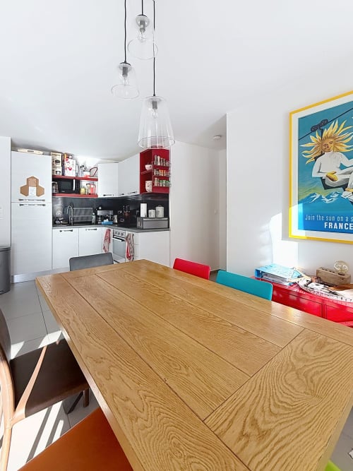 Cuisine-salle à manger moderne avec table en bois, chaises rouges et bleues, suspensions luminaires et affiche vintage colorée à Montgenèvre
