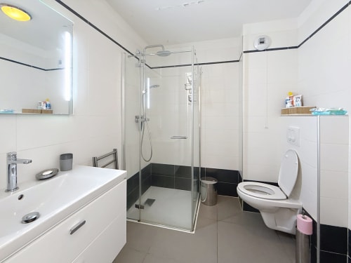 Salle de bains moderne avec douche à l'italienne, vasque blanche, toilettes et accents de carrelage noir à l'appartement Les Tanières de Montgenèvre
