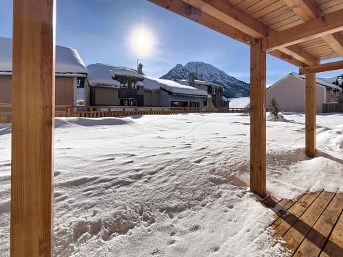 Cour enneigée des Tanières de Montgenèvre avec chalets en bois et vues sur les sommets montagneux enneigés