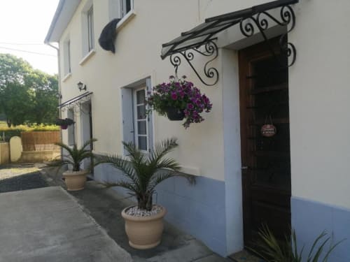 Entrada encantadora da Pousada Maison de Barlest com flores roxas pendentes e toldo decorativo em ferro forjado