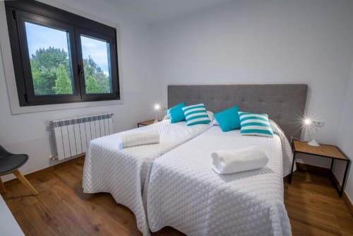 Habitación moderna en el hotel Bikarte con almohadas turquesas, ropa de cama blanca, cabecero gris y vistas al bosque