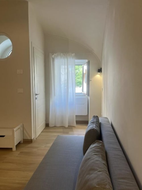 Spaziosa camera al piano terra di Marelia Suites a Vasto con divano grigio, pavimenti in legno, soffitto voltato e porta aperta verso il balcone