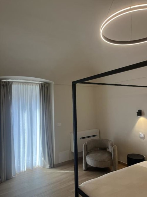 Camera moderna presso Marelia Suites a Vasto con letto a baldacchino, plafoniera neon, tende grigie e sedia contemporanea