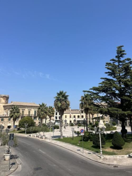Vista della piazza del paese di Vasto dal balcone di Marelia Suites con palme ed edifici storici sotto il cielo azzurro