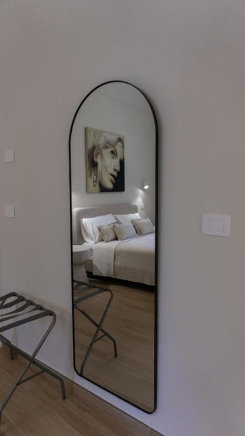 Specchio ad arco alto in camera doppia Marelia Suites che riflette la camera da letto con letto bianco e quadro ritratto