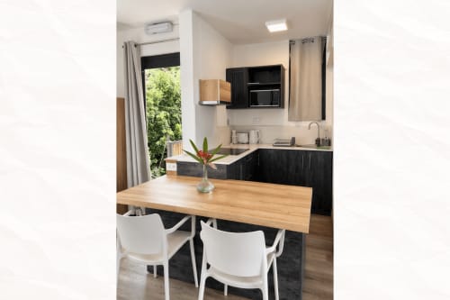 Modern kitchen-dining area at Joubarbe Résidence, Moka. Black cabinetry, wooden table, white chairs, mountain views through