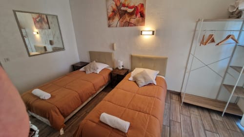 Chambre twin de l'Hôtel Du Nord Cannes avec literie orange, têtes de lit neutres, œuvres d'art murales, miroir et équipements modernes