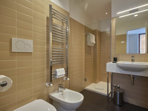 Bagno moderno nella Deluxe Junior Suite di Portica Homes ad Assisi con scaldasalviette, doccia, bidet e piastrelle color sabbia