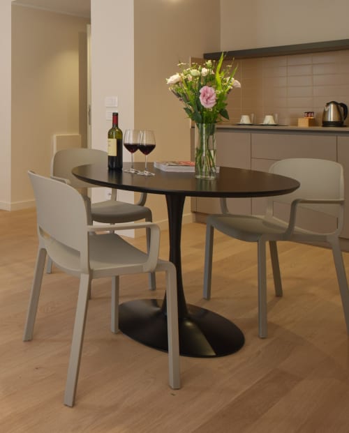 Moderna sala da pranzo in hotel ad Assisi con tavolo ovale nero, sedie grigie, calici di vino e fiori freschi con vista sulla città