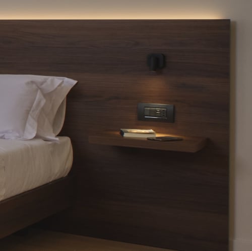 Testata del letto in legno scuro con cuscini bianchi, comodino con lampada e telefono presso l'hotel Portica Homes Assisi