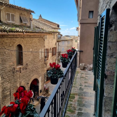 Via medievale in pietra ad Assisi con fiori rossi al balcone di Portica Homes B&B
