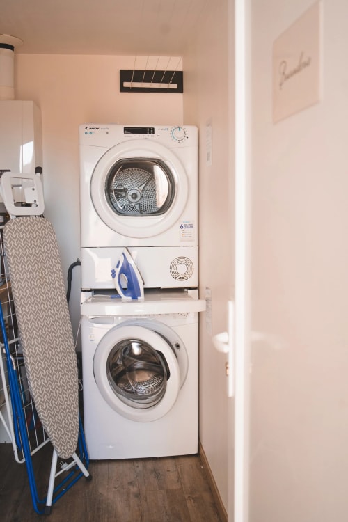 Laundry room at Résidence des Sables with stacked washer and dryer, ironing board, and wall-mounted drying rack