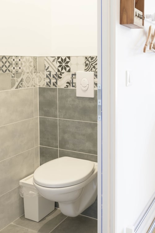 Modernes Badezimmer mit wandhängendem Toilettensitz, gemusterter Fliesenbordüre und grauen Fliesenerwänden im Ferienhaus Domaine Le Piboul