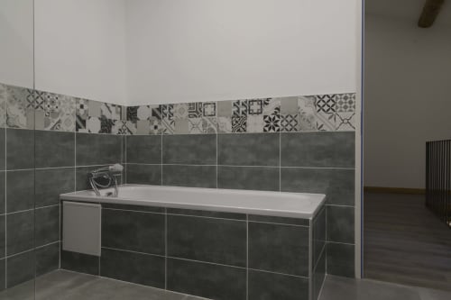 Modernes Badezimmer im Ferienhaus Domaine Le Piboul in Fontcouverte mit dunklen Fliesen, dekorativen Bordürenfliesen und weißer Badewanne