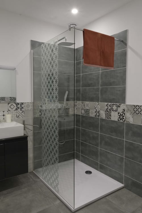 Modernes Badezimmer mit offener Dusche, grauen Fliesen und dekorativer weißer gemusterter Akzentwand im Cottage Domaine Le Piboul