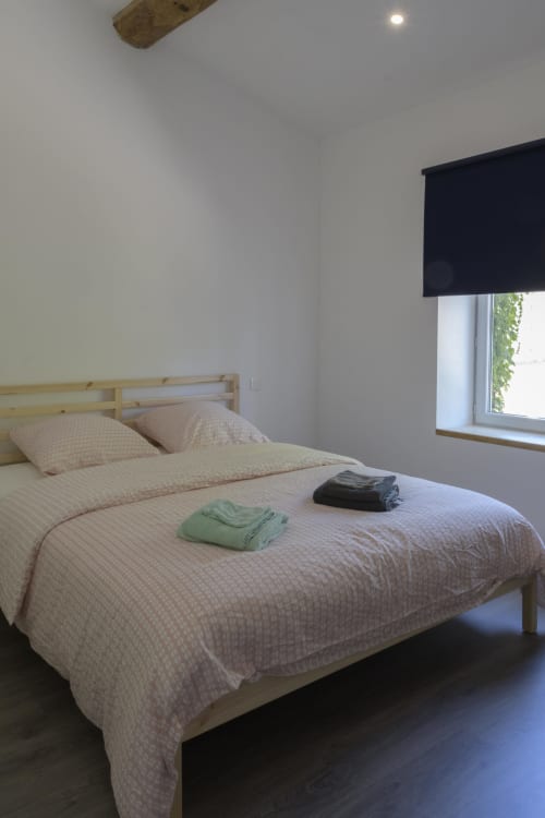 Helles Schlafzimmer mit Holzbett, beigen Betttüchern und schwarzem Fensterrollo im Cottage Domaine Le Piboul in Fontcouverte