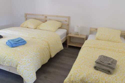 Leuchtend gelbe gemusterte Bettwäsche im Schlafzimmer des Landhauses Domaine Le Piboul, Fontcouverte, mit Holzbetten und dunklem Boden