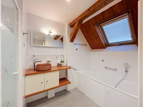 Salle de bains moderne à La Wantzenau avec poutres en bois, lavabo en terre cuite, carrelage blanc et fenêtre de toit.