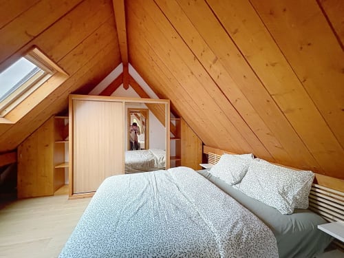 Chambre spacieuse sous les toits avec poutres apparentes, lit queen-size, armoire et lucarne dans l'appartement de La Wantzenau