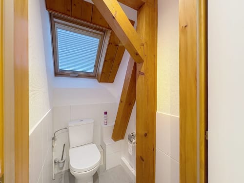 Salle de bain moderne avec puits de lumière, poutres en bois, sanitaires blancs et porte-brosse WC, appartement La Wantzenau