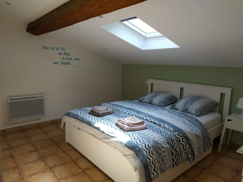 Helles Dachschlafzimmer im Domaine Le Piboul mit Dachfenster, weißem Bett, gestreifter Bettwäsche, grüner Akzentwand und Holzbalken