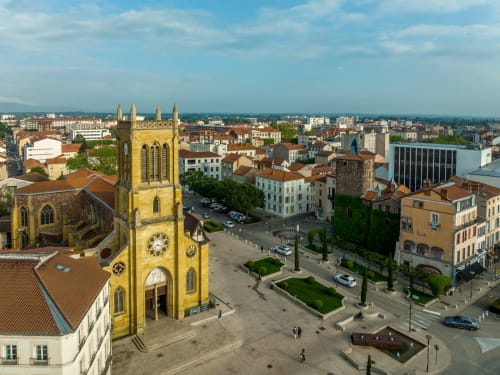 Aerial view of Mably's historic yellow church and town square with residential buildings and mountains beyond