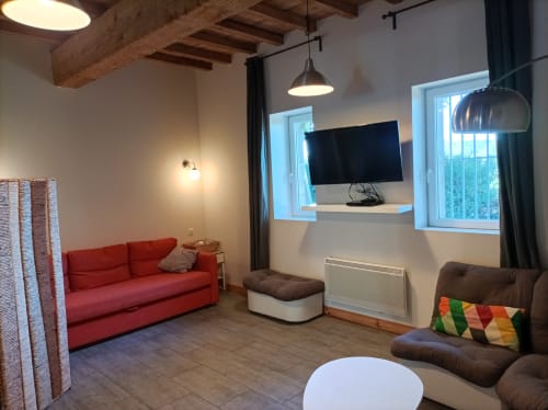 Modernes Wohnzimmer des Landhauses Domaine Le Piboul mit rotem Sofa, braunem Sessel, Flachbildfernseher, sichtbaren Balken und Garten