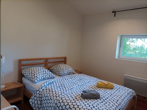 Helles Schlafzimmer im Domaine Le Piboul mit Holzbett, blauem gemustertem Bettzeug und Fensterblick auf den Garten