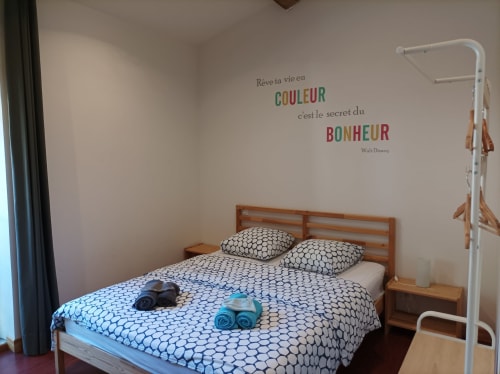 Gemütliches Schlafzimmer im Domaine Le Piboul mit Holzbett, gemusterter Bettwäsche und inspirierendem französischem Wandzitat über Farbe