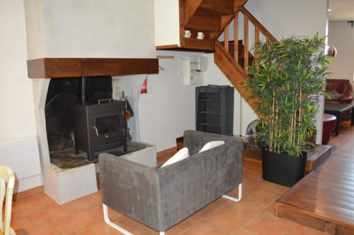 Wohnzimmer des Cottages im Domaine Le Piboul mit Holztreppe, Kamin, grauem Sessel und Topfpflanze