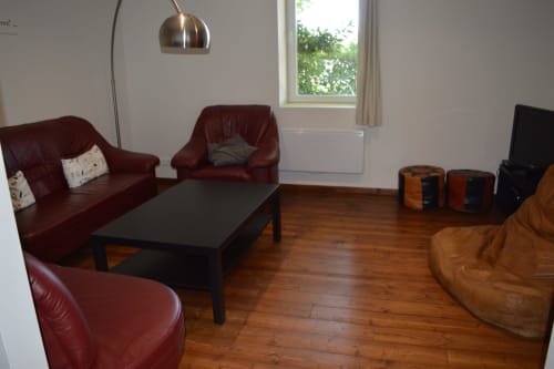 Geräumiges Cottage-Wohnzimmer mit burgunderrotem Ledersitzen, schwarzem Couchtisch, Holzböden und Gartenblick