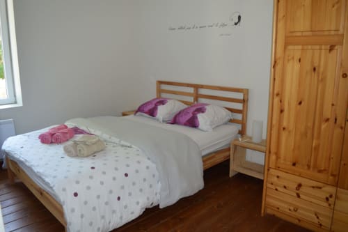 Geräumiges Schlafzimmer des Cottages Le Régisseur, Domaine Le Piboul, mit Holzbett, violetten Kissen und Kiefernmöbeln