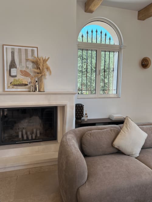 Salon moderne M Résidences avec fauteuil beige, cheminée et baie vitrée cintrée donnant sur la verdure