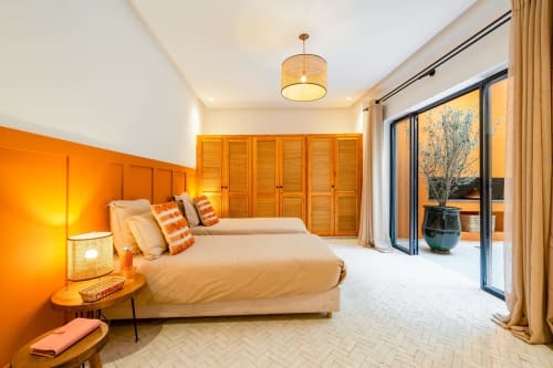 Chambre moderne aux M Résidences et Hôtels avec mur d'accent orange vibrant, lits jumeaux, armoires en bois et patio coulissant