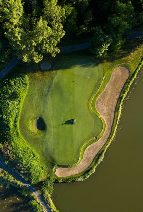 Vue aérienne d'un parcours de golf aux greens entretenus, bunkers de sable et plans d'eau entourés d'arbres luxuriants