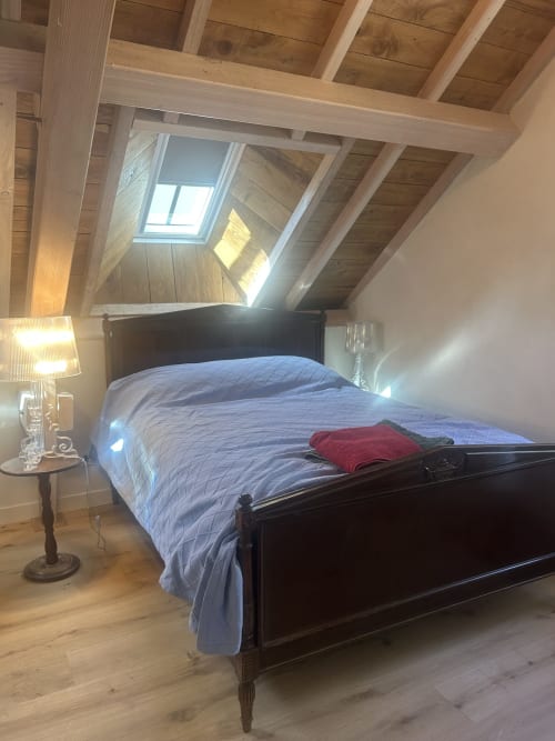 Chambre cosy du Studio à la Cour Du Liège avec lit en bois foncé, verrière, poutres apparentes et vue sur le jardin