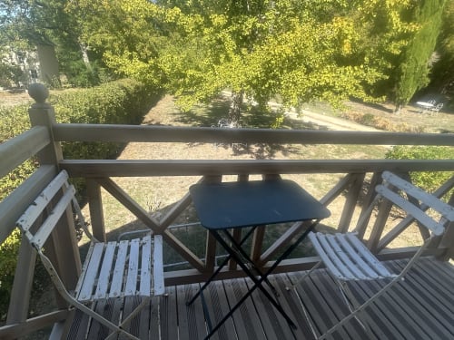Terrasse en bois avec chaises blanches et petite table surplombant les jardins luxuriants du gîte Cour Du Liège à Baugé-en-Anjou