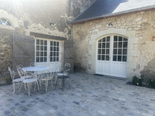 Cour pavée en pierre à la Cour Du Liège avec mobilier en fer forgé blanc et portes-fenêtres cintrées donnant sur le jardin