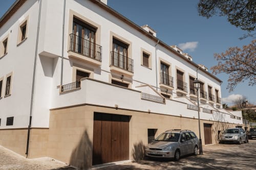 Exterior de Apartamentos Estrella Baeza con fachada blanca, puertas de garaje de madera y vehículos estacionados en Baeza