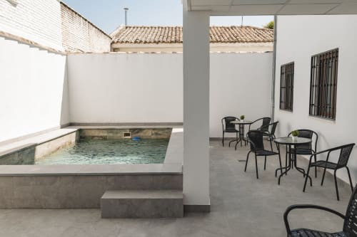 Patio de Apartamentos Estrella Baeza con pequeña piscina, sillas metálicas negras y paredes blancas en Baeza, España