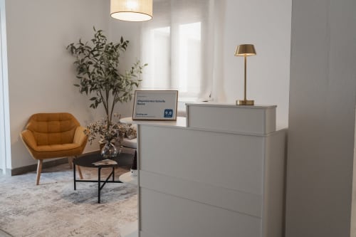 Moderna recepción de Apartamentos Estrella Baeza con escritorio gris, silla naranja e iluminación natural abundante