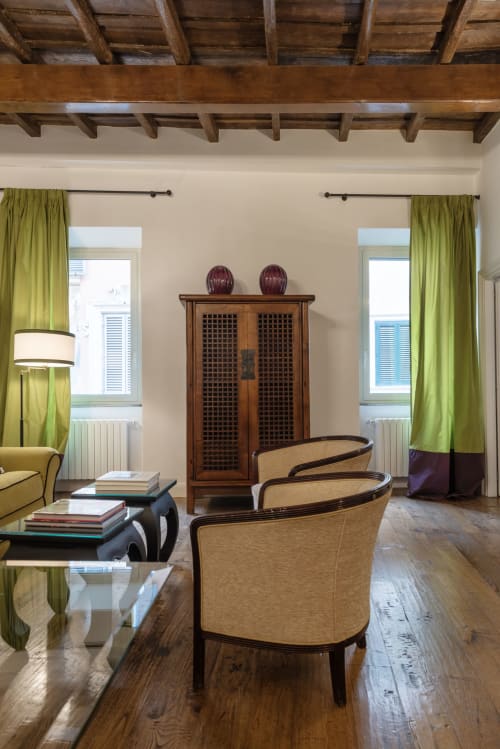 Elegante salotto a Residenza Clodio Roma con travi in legno a vista, tende verdi, poltrone beige e vista sulla città
